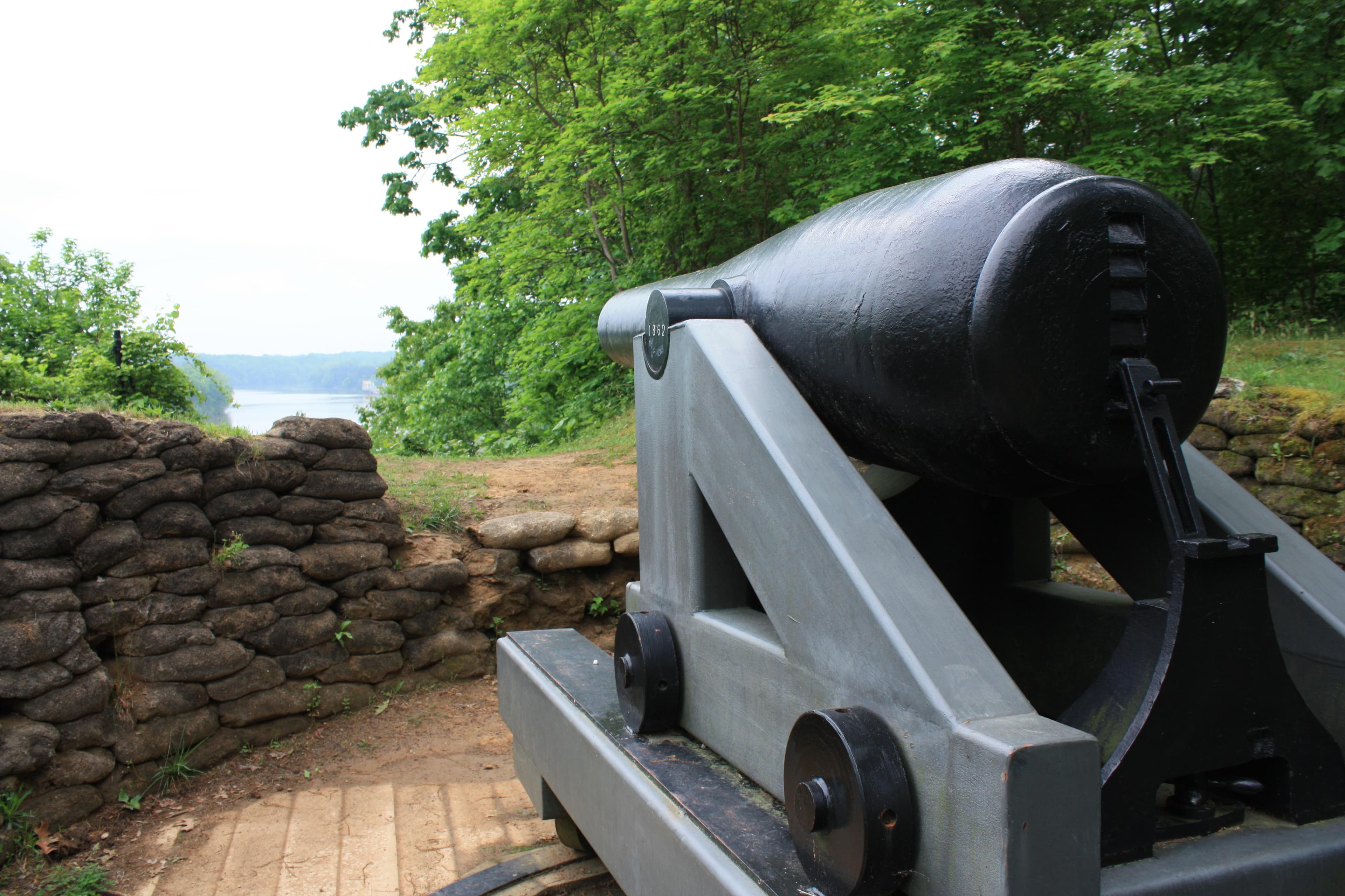 A large, black Civil War cannon overlooking a river from a high bluff.