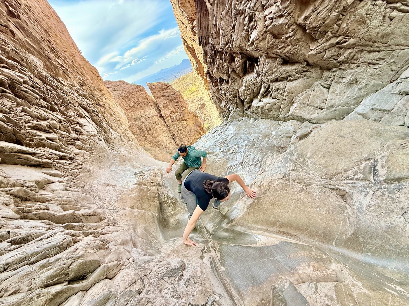 A hiker climbing back up the smooth, water-eroded rock at the lip of the Window, the precipitous drop visible behind, Big Bend National Park