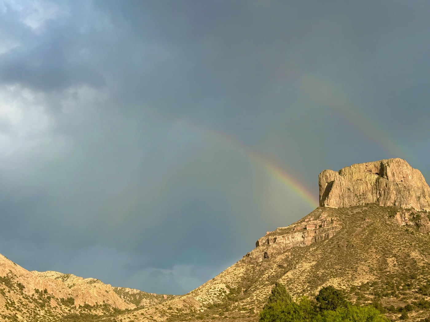 A double rainbow arched over a striking Big Bend rock feature against a darkening storm sky — the rare desert storm caught at its most vivid
