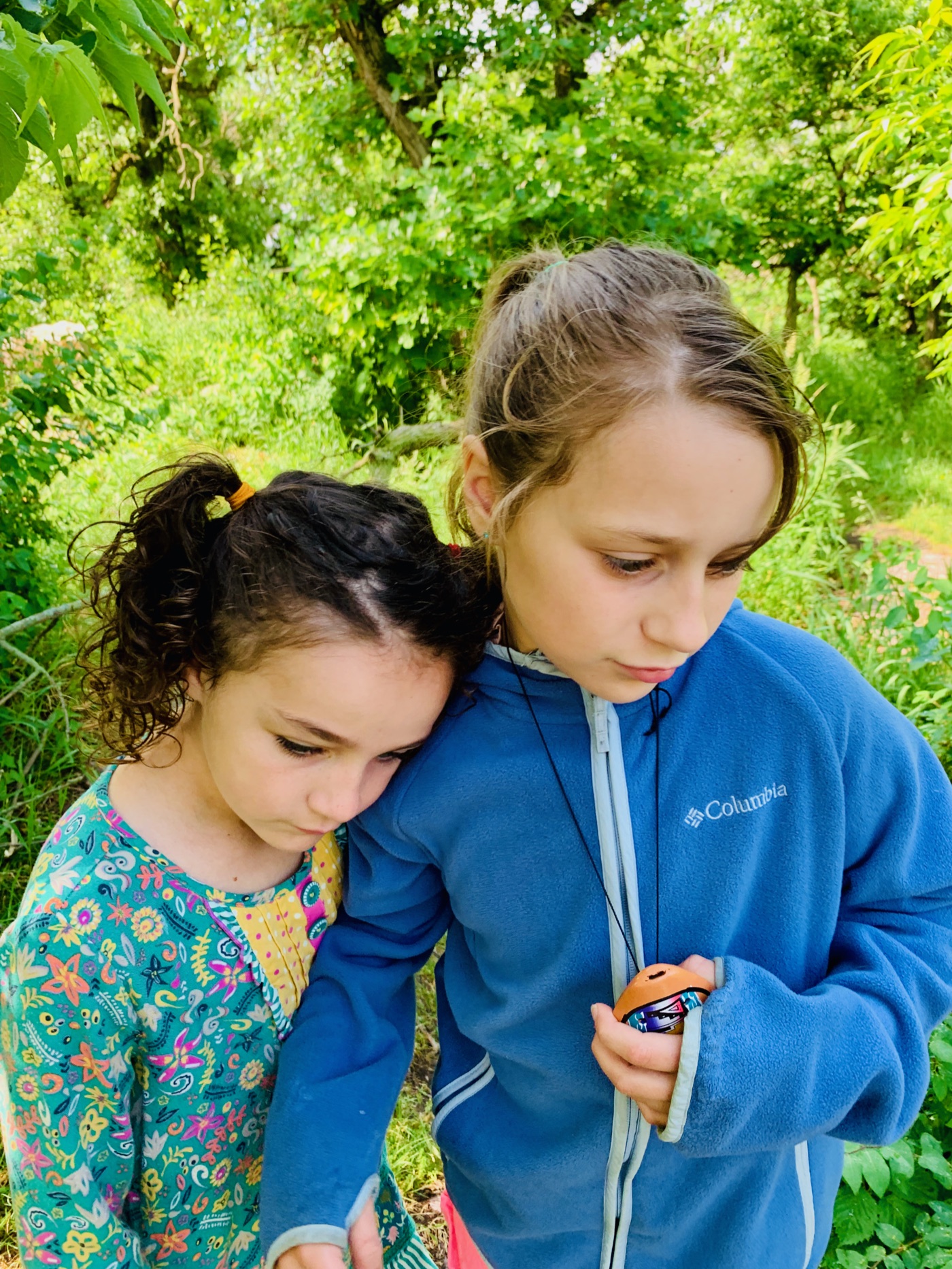 Two young sisters, heads leaned together, quiet on the trail
