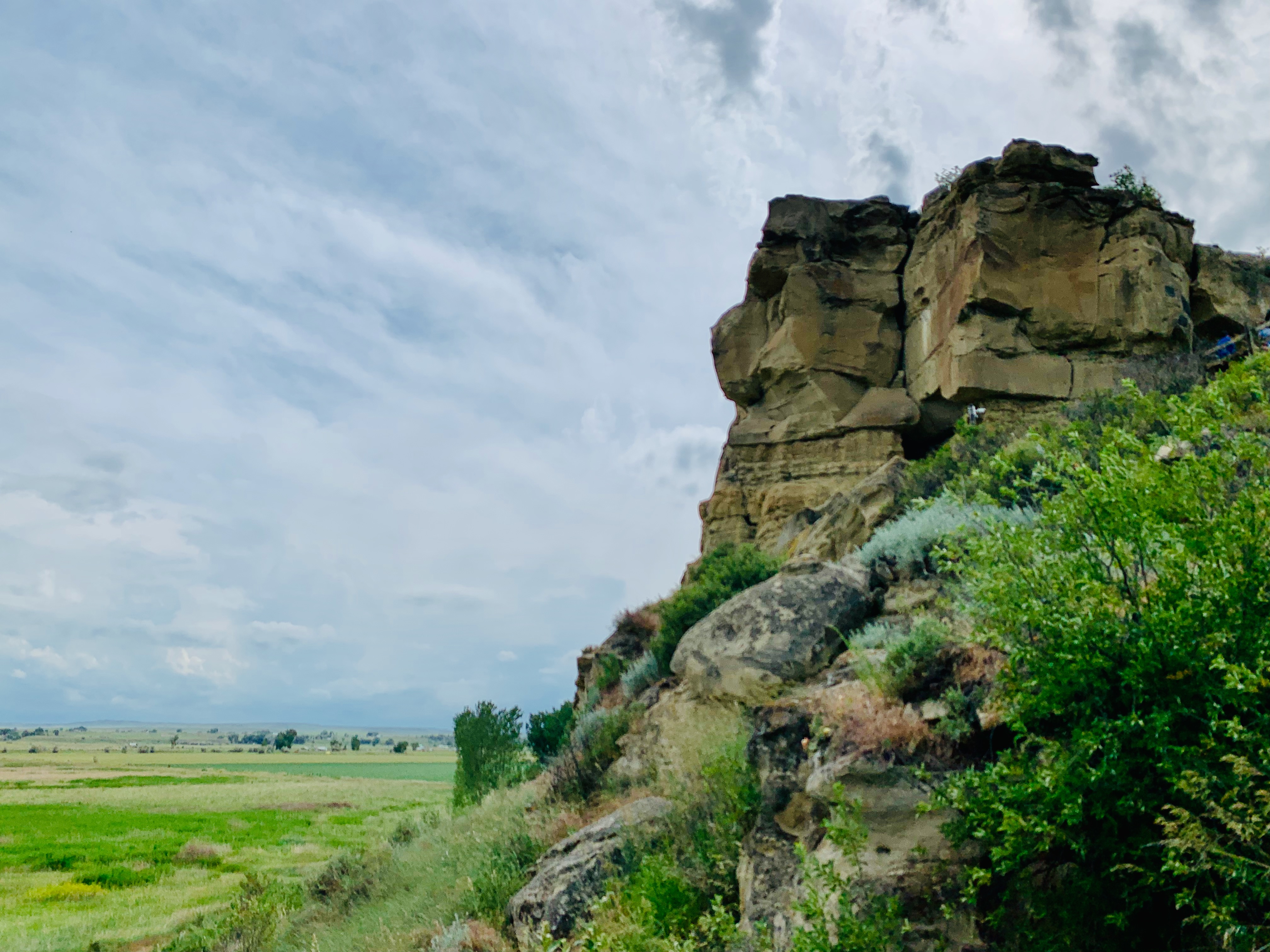 The sandstone pillar rising out of the green Yellowstone River valley under a wide Montana sky