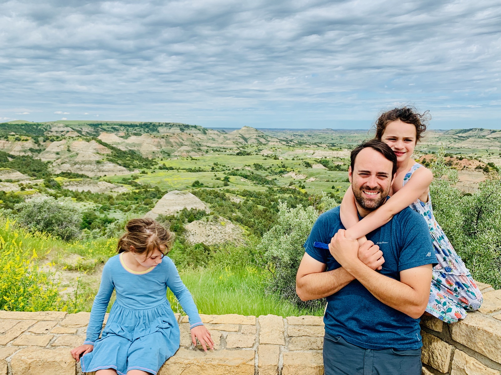 Dad and daughters at the stone overlook wall, yellow sweetclover blooming along the badlands rim
