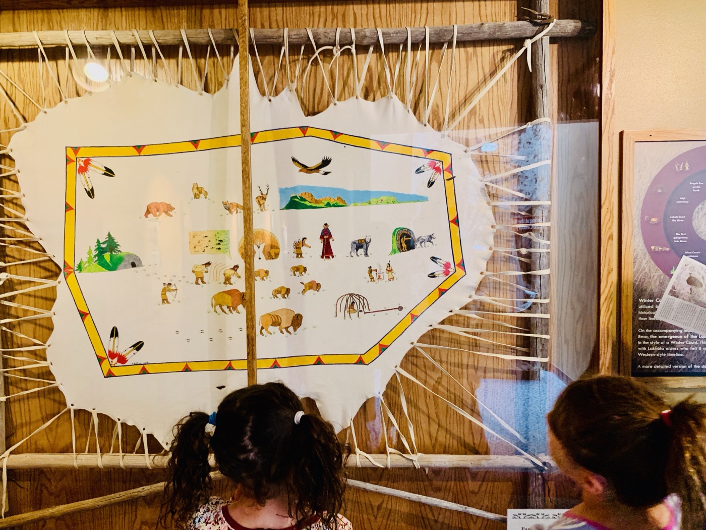 The girls reading the painted buffalo-hide that tells the emergence story in pictures