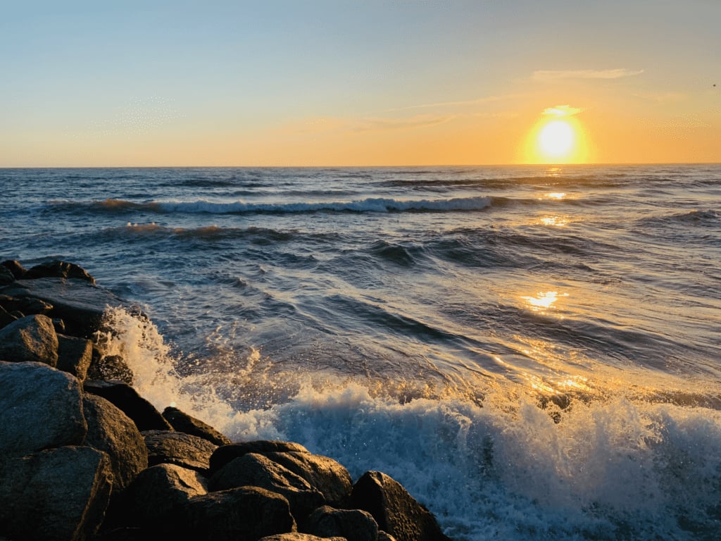 Blue waves crashing against rocks at Sunset Moss Landing State Beach with golden sunset in the background