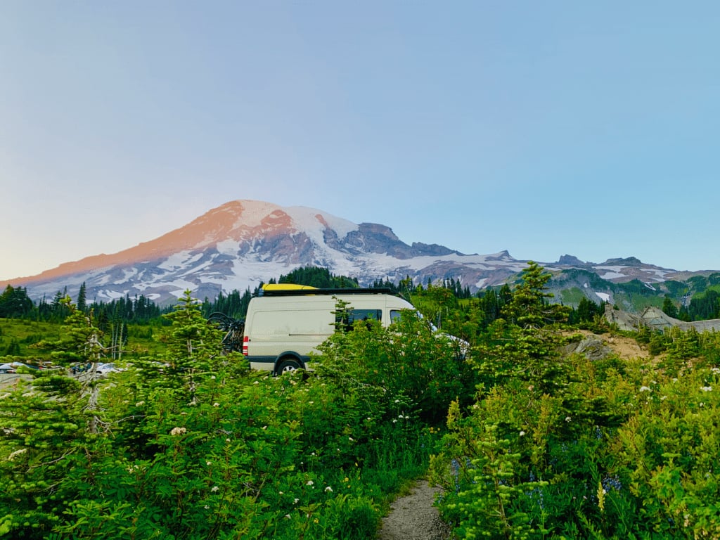 Van is the Best Summer Camper with yellow kayak on the top parked in Paradise with greenery and Mount Rainier in the background