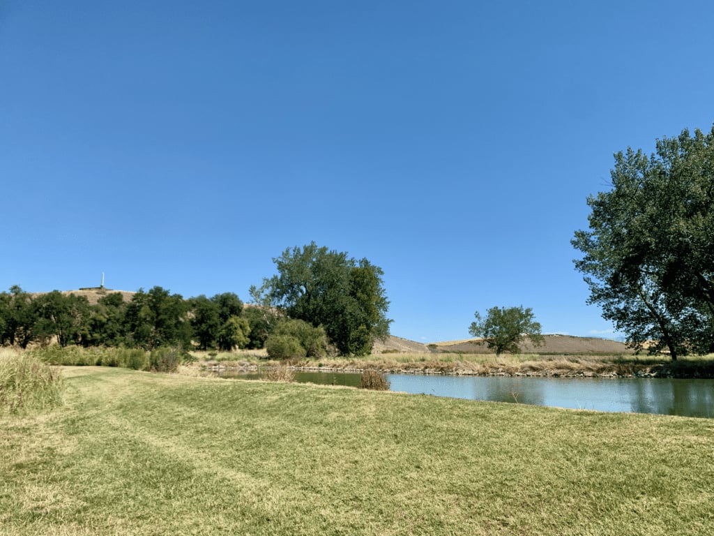 Whitman Mission Historic Site with Memorial on top of hill and lake and deciduous trees with clear skies in the background